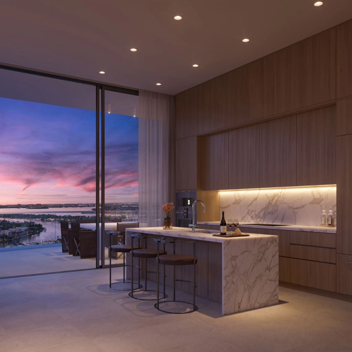 Modern kitchen with marble island and bar stools, opening to a balcony with a sunset view.