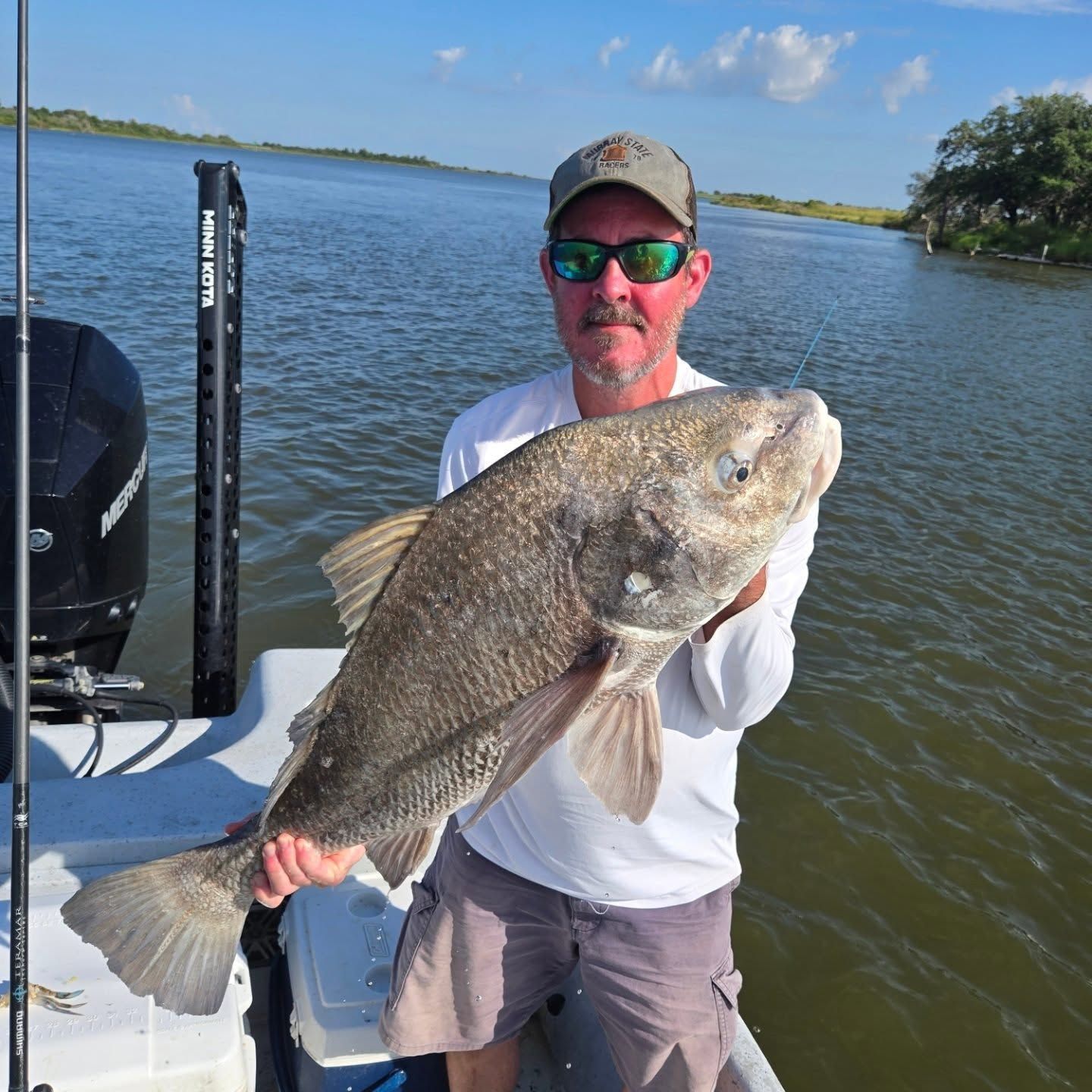 Angler on a boat holding a large fish on a sunny lake.