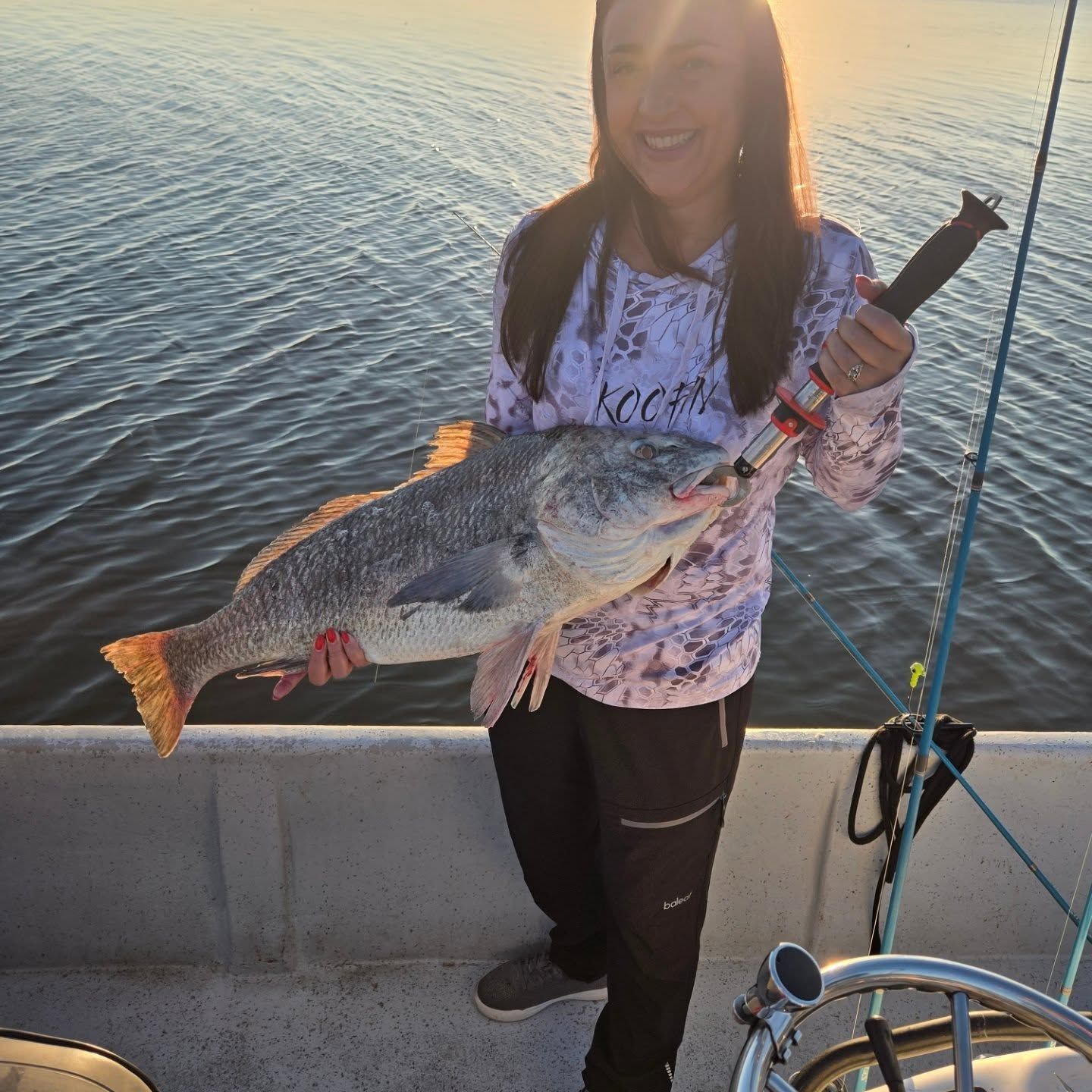 Person on a boat holding a large fish over the water at sunset
