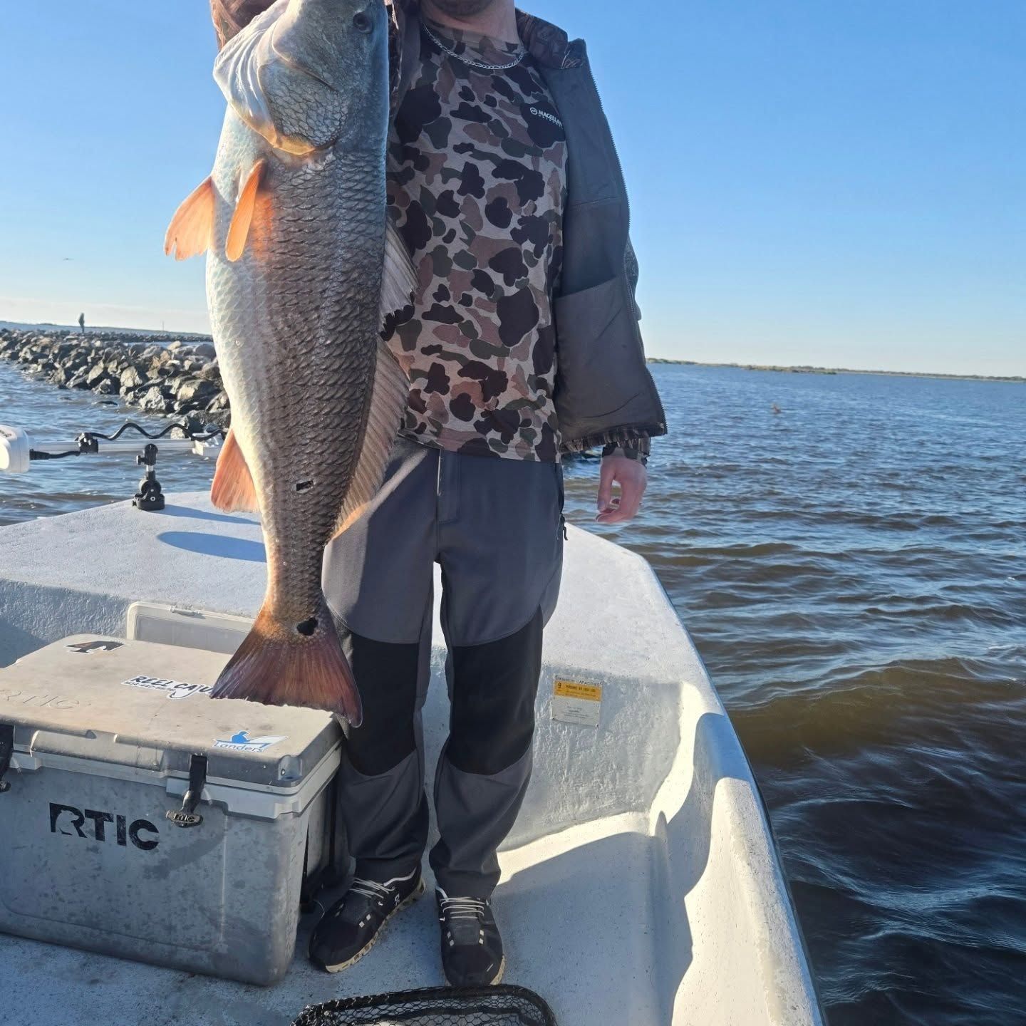 Person on a boat holding a large fish over a cooler on open water.
