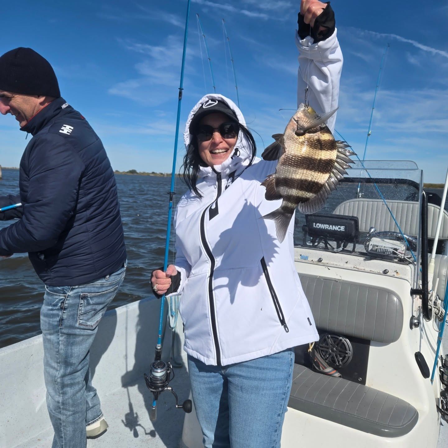 Person on a boat holding a fishing rod and a striped fish, smiling in bright sunlight.