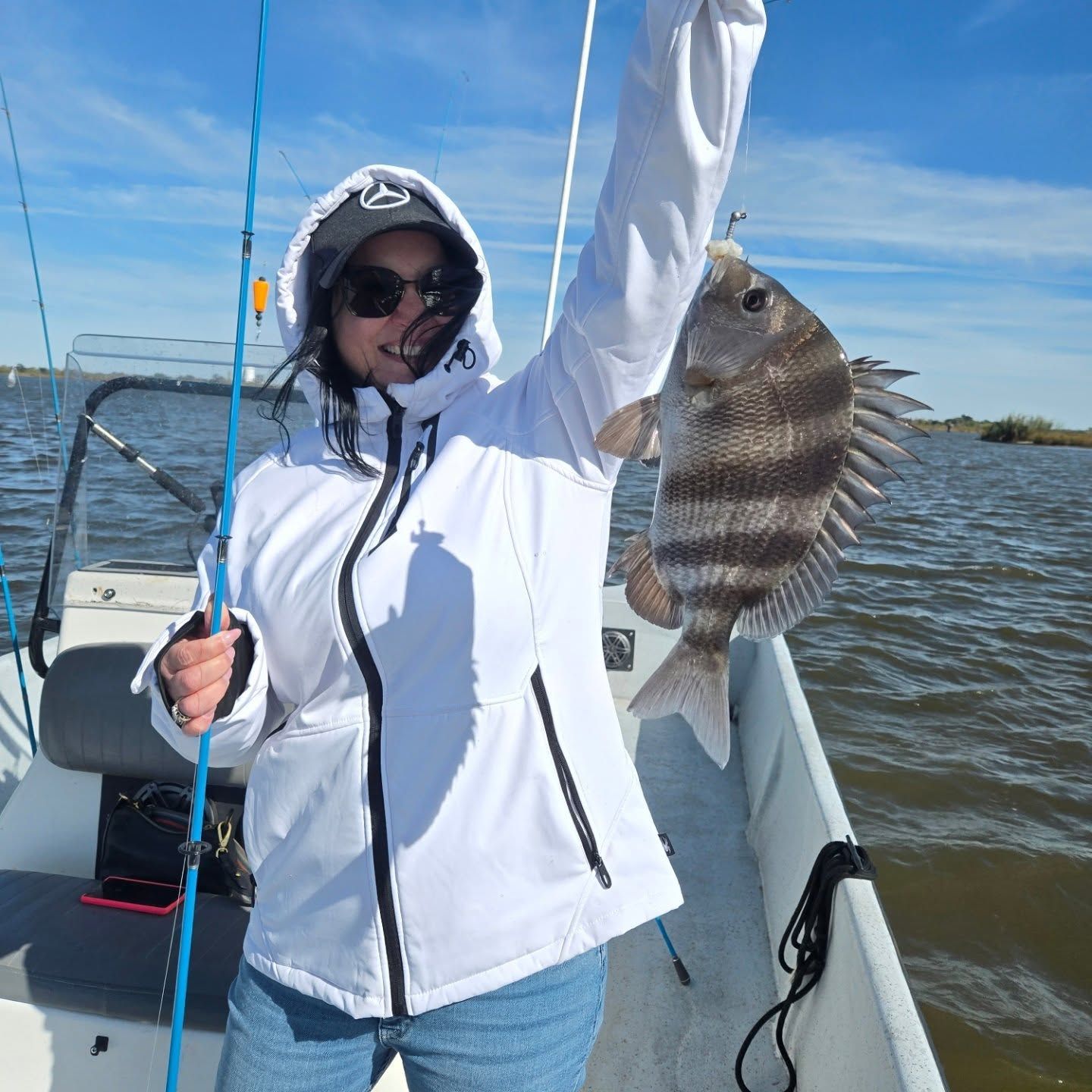 Person on a boat holding up a striped fish on a sunny day