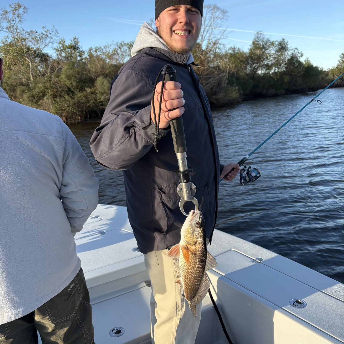 Angler smiling while holding a fish on a boat during a sunny day.
