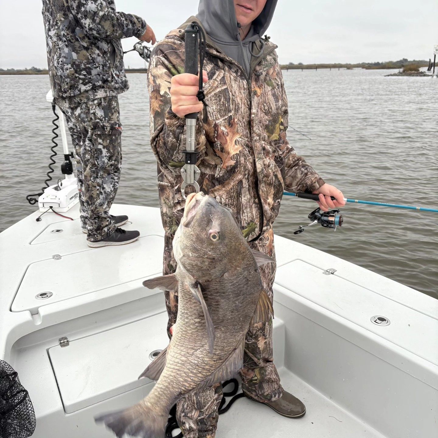 Angler on a boat holds a large fish over the deck on a cloudy day