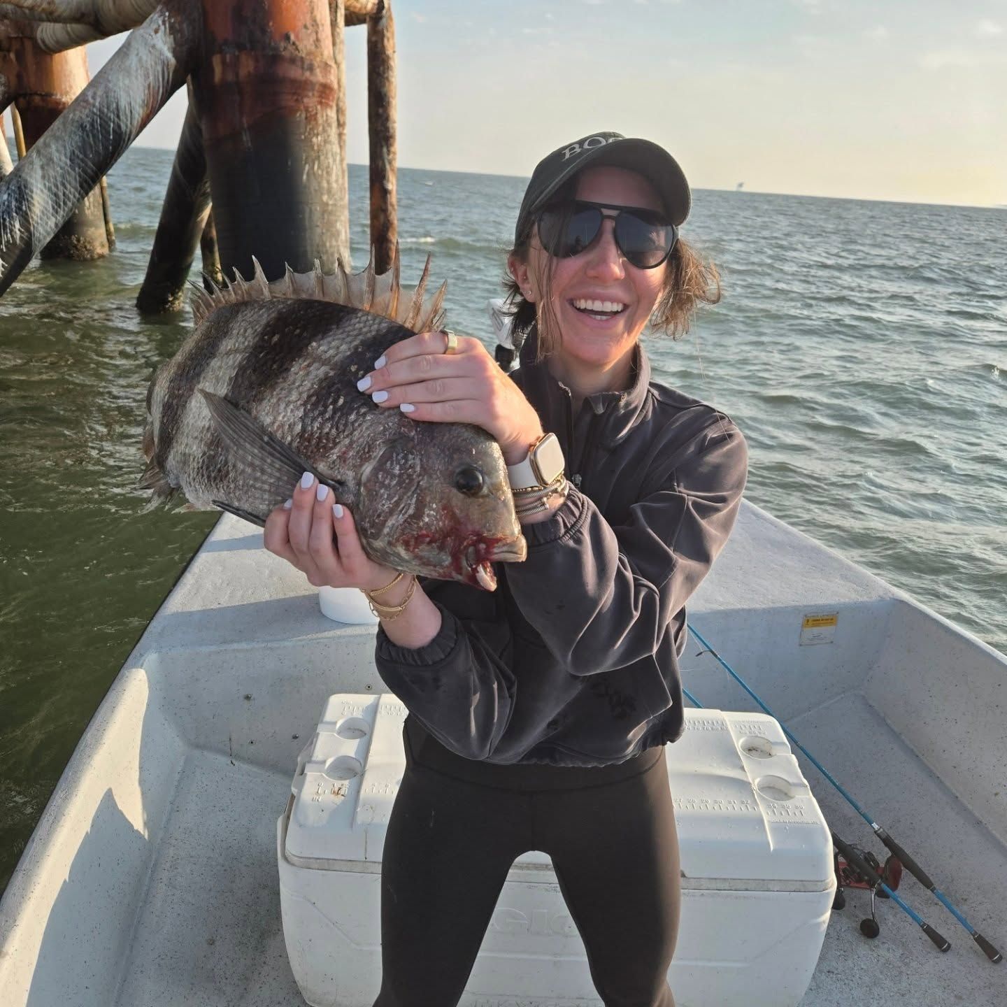 Person on a boat holding a large striped fish, smiling near a pier at sunset
