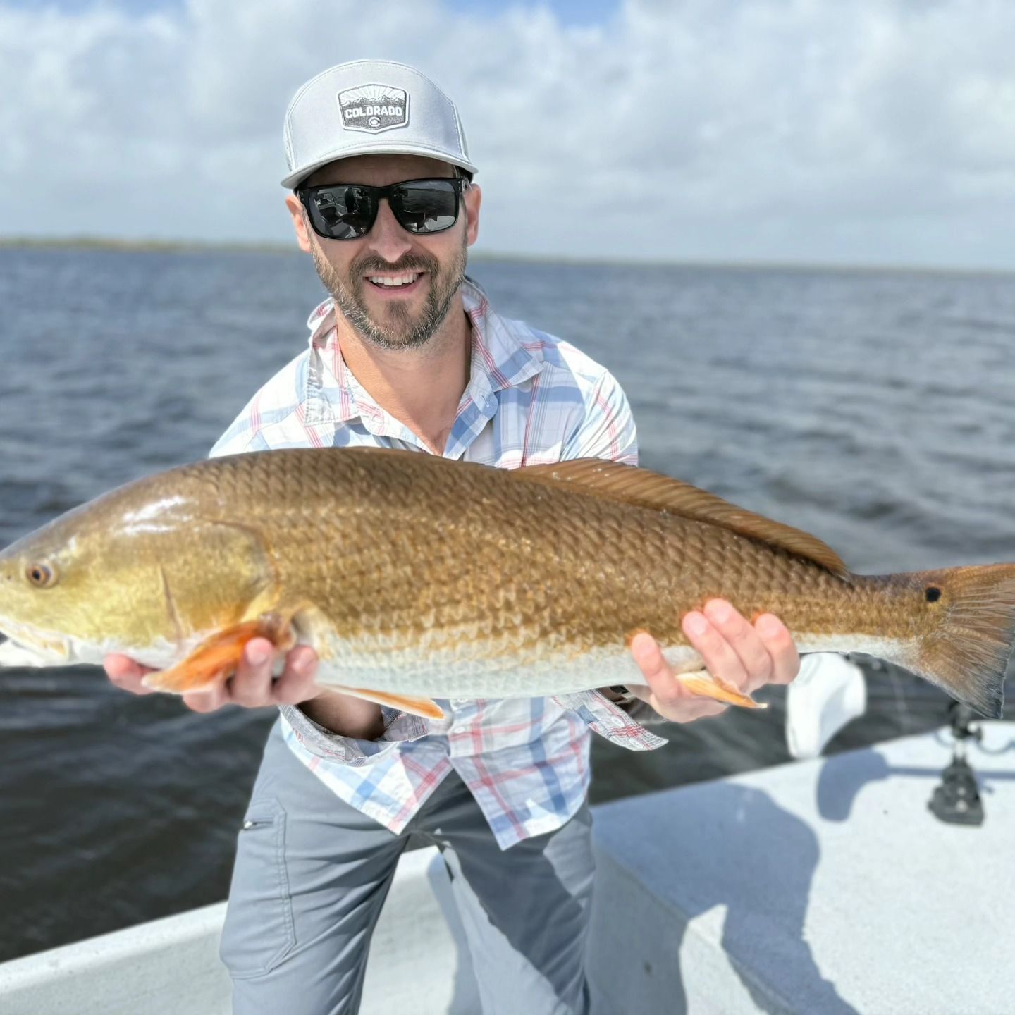 Smiling angler on a boat holding a large brown fish over the water.