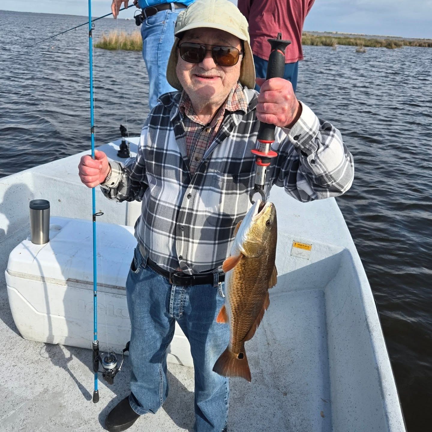 Smiling person on a boat holds a fishing line and a large fish on a sunny lake