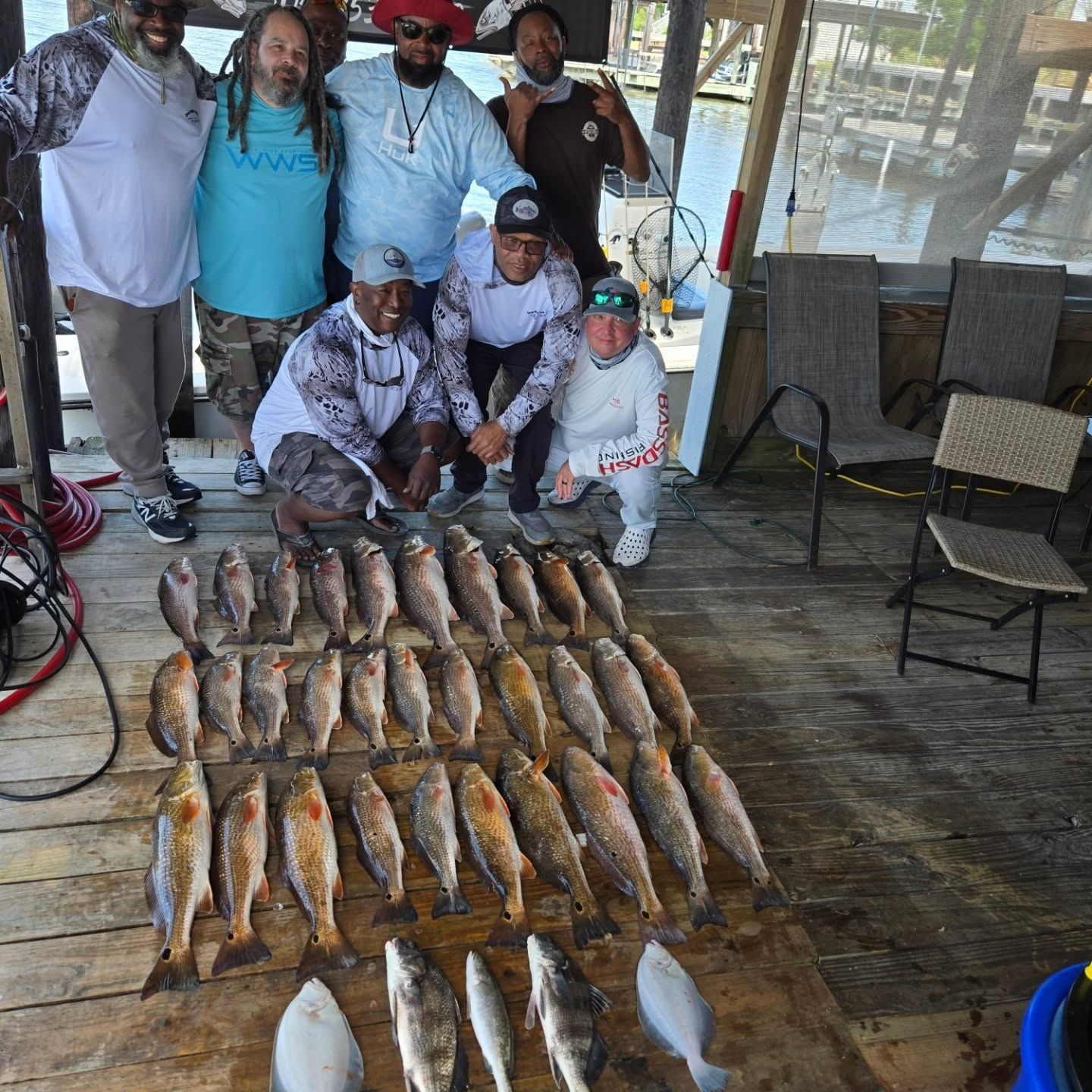 Group posing beside rows of freshly caught fish laid out on a wooden deck at a waterfront dock