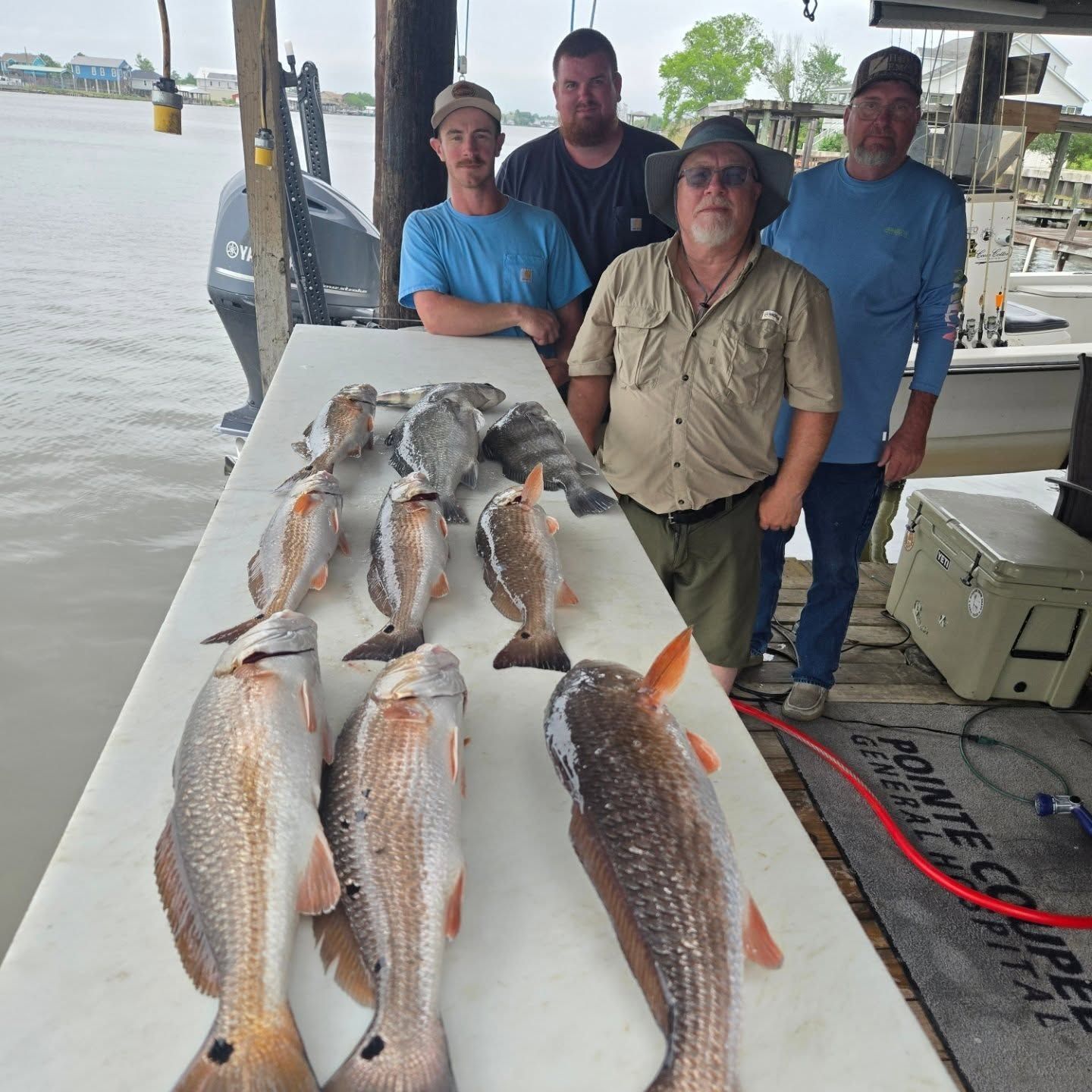 Four people posing beside a table of freshly caught fish on a dock by the water