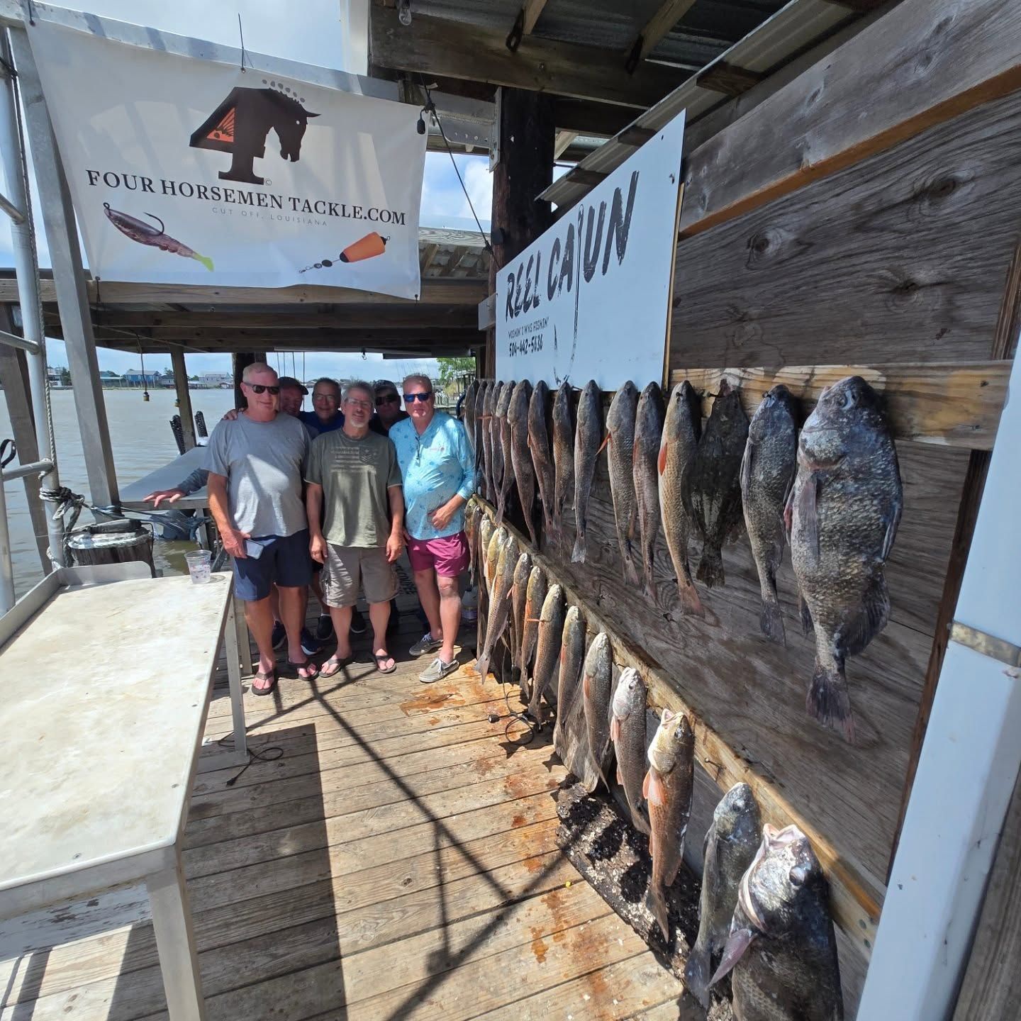 Four people posing beside rows of hanging fish at a dockside fish cleaning station