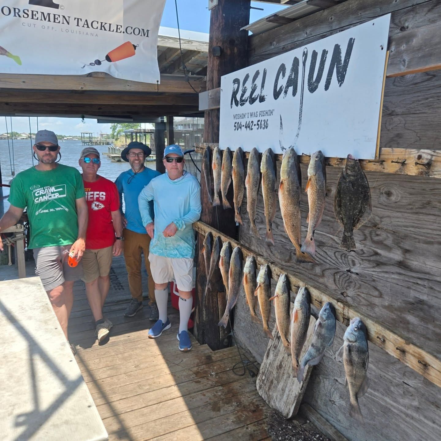 Four people posing beside a fish display and sign at a rustic dockside market.