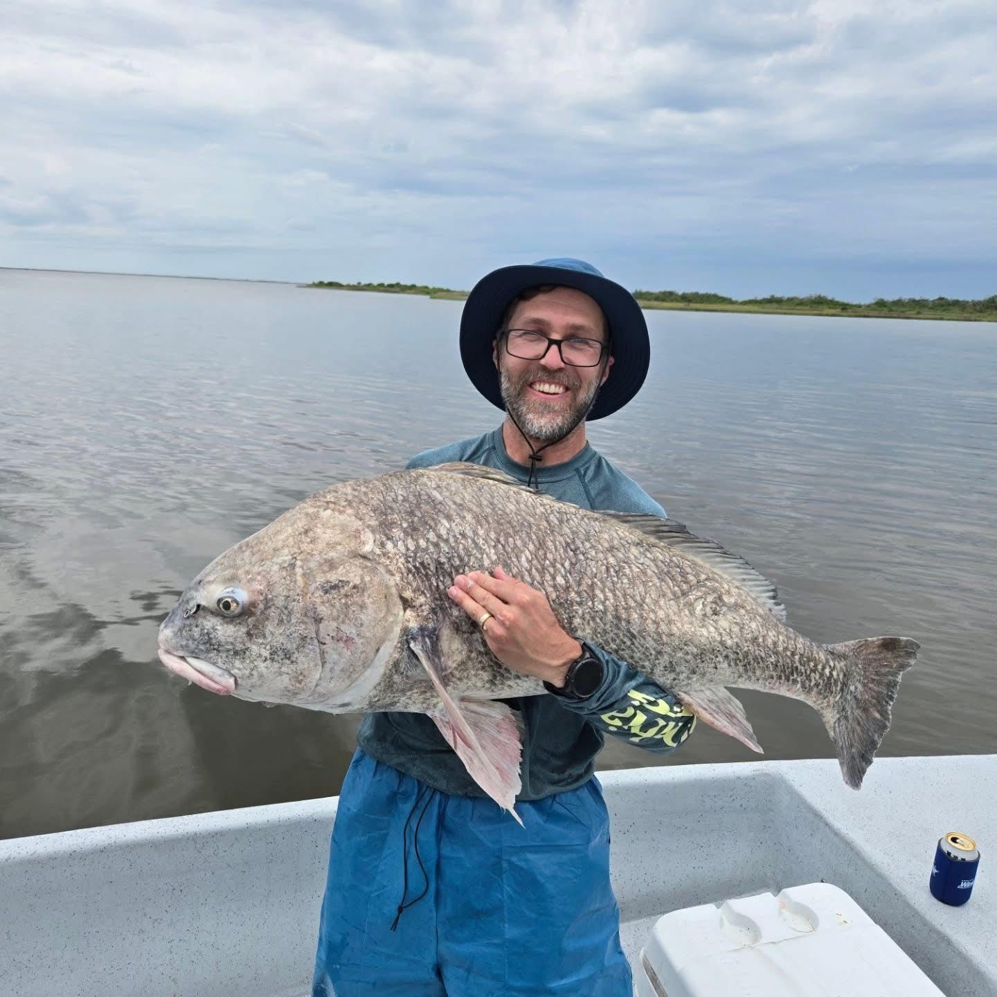 Man holding a large fish on a boat in calm water under a cloudy sky