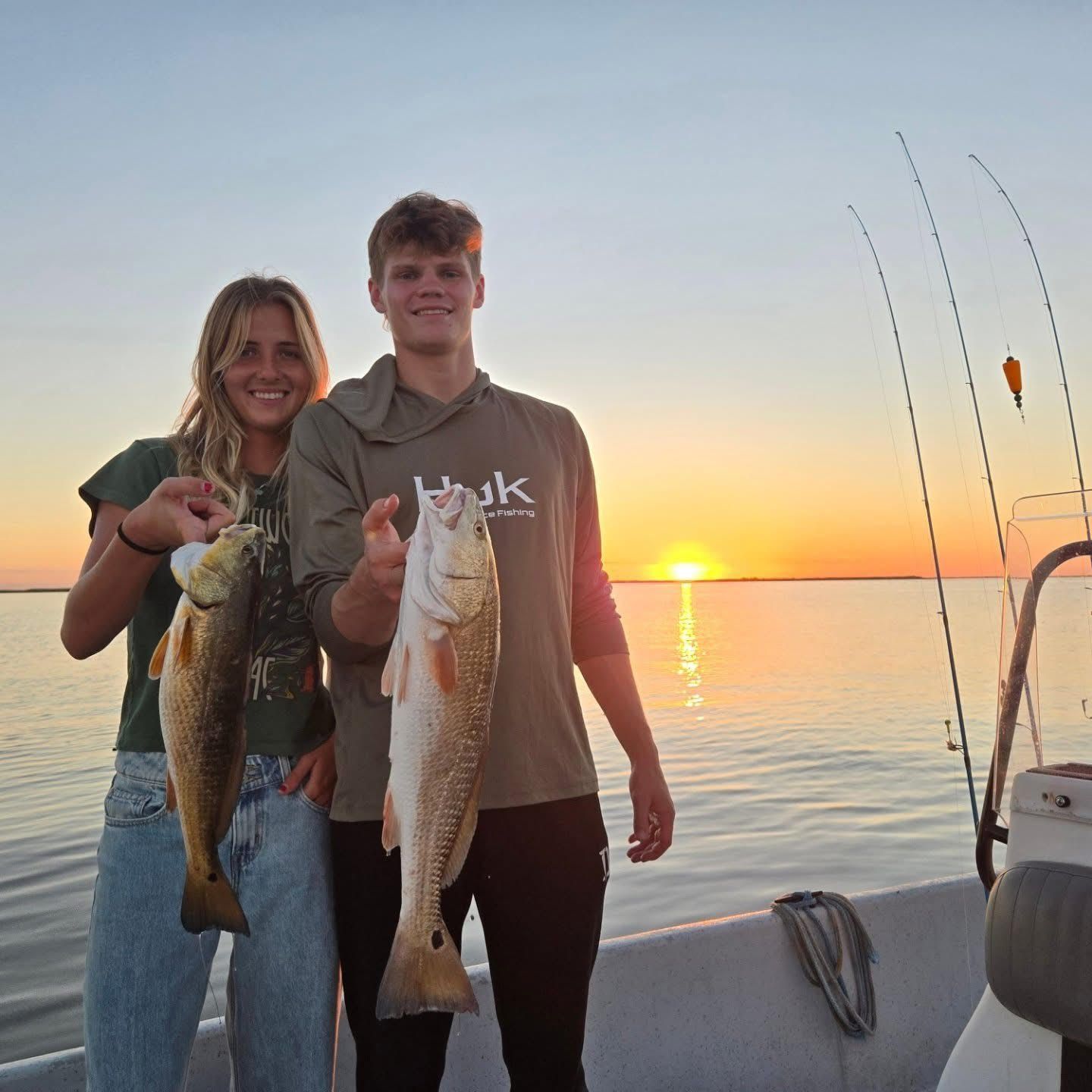 Two people on a boat holding fish at sunset on calm water