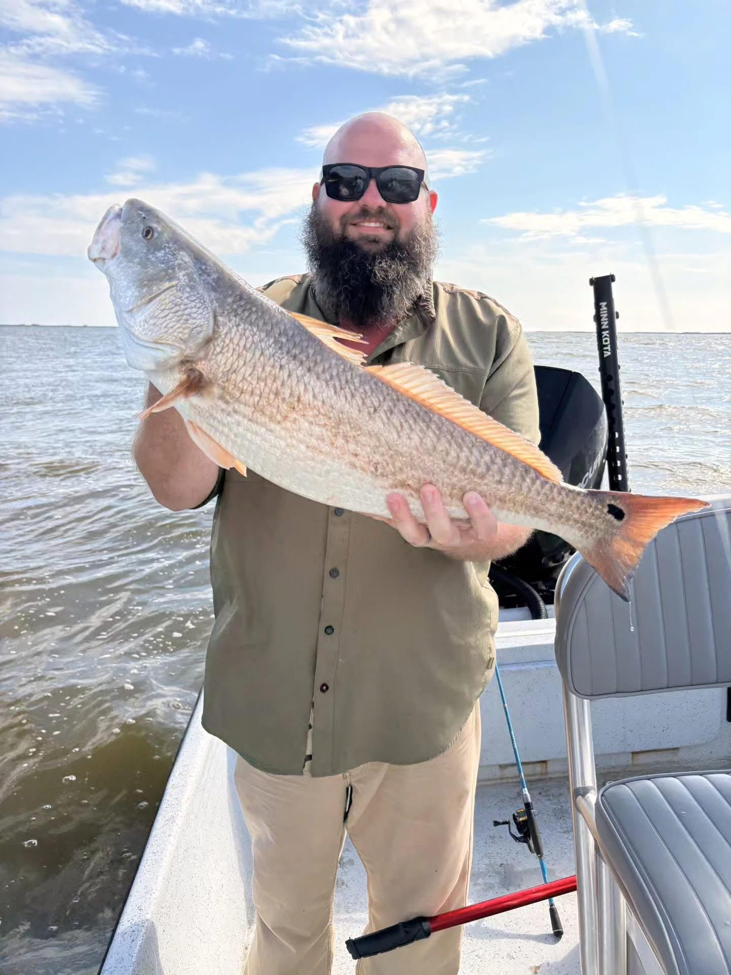 Man holding a large silver fish on a boat under a bright blue sky