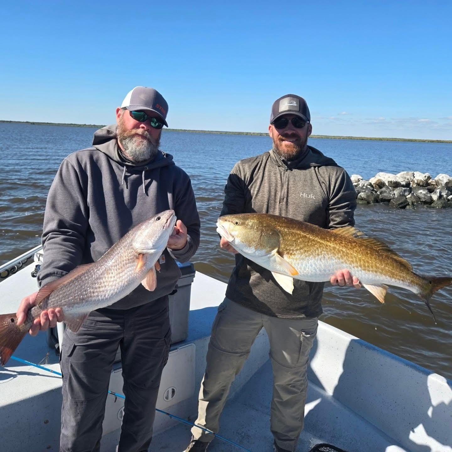 Two anglers on a boat holding large fish on a sunny lake
