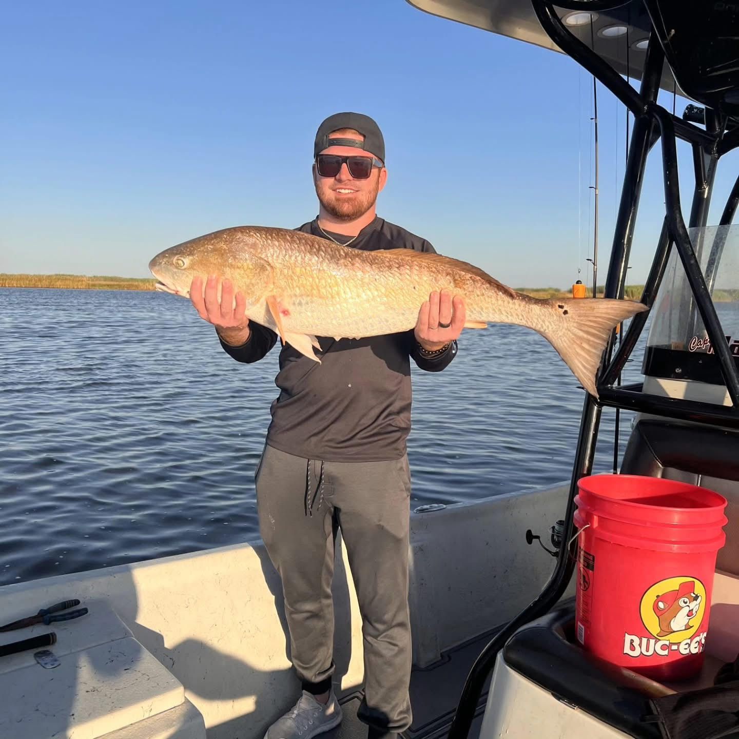 Person on a boat holding a large fish over calm water at sunset