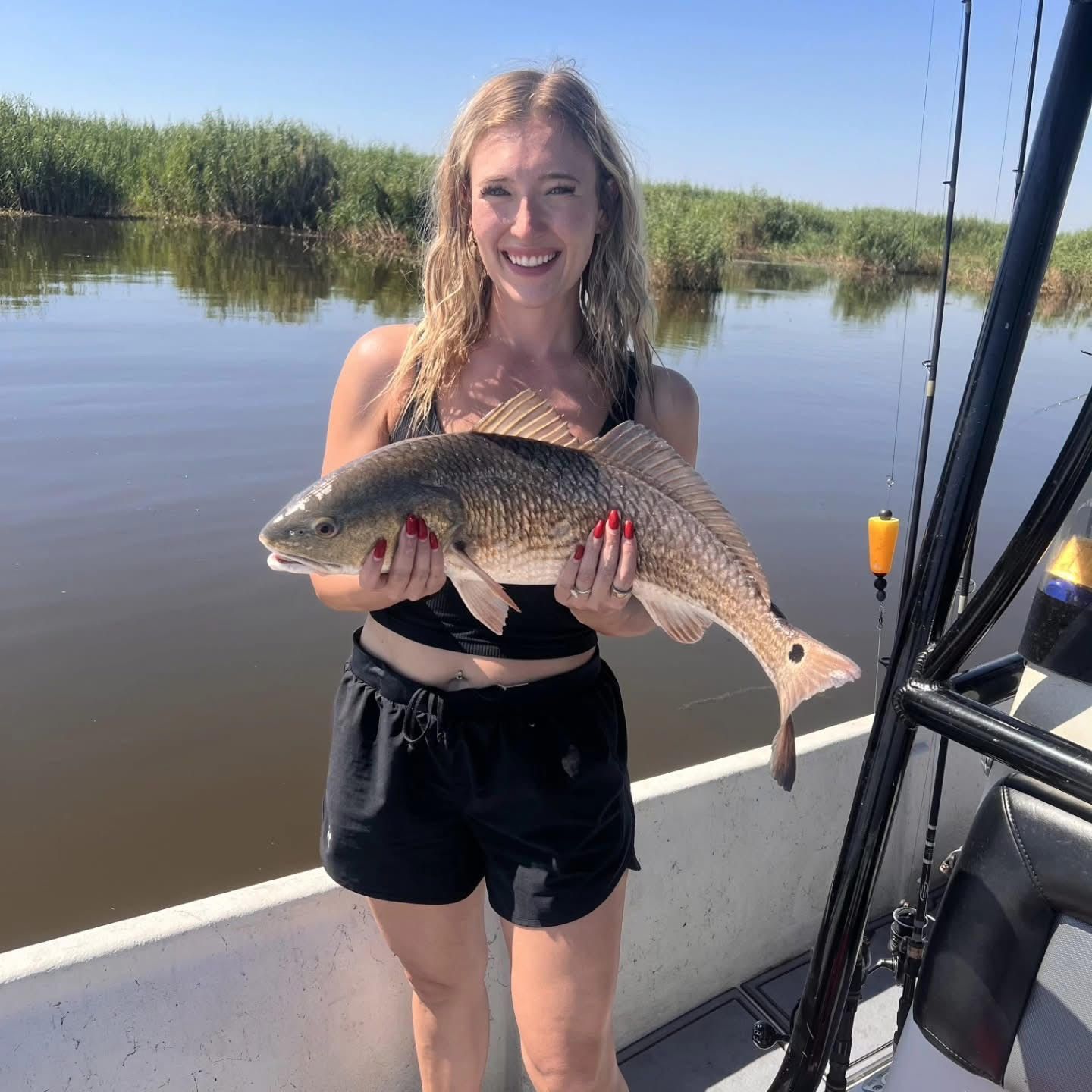 Smiling angler holding a large fish on a boat in calm water near marsh grass