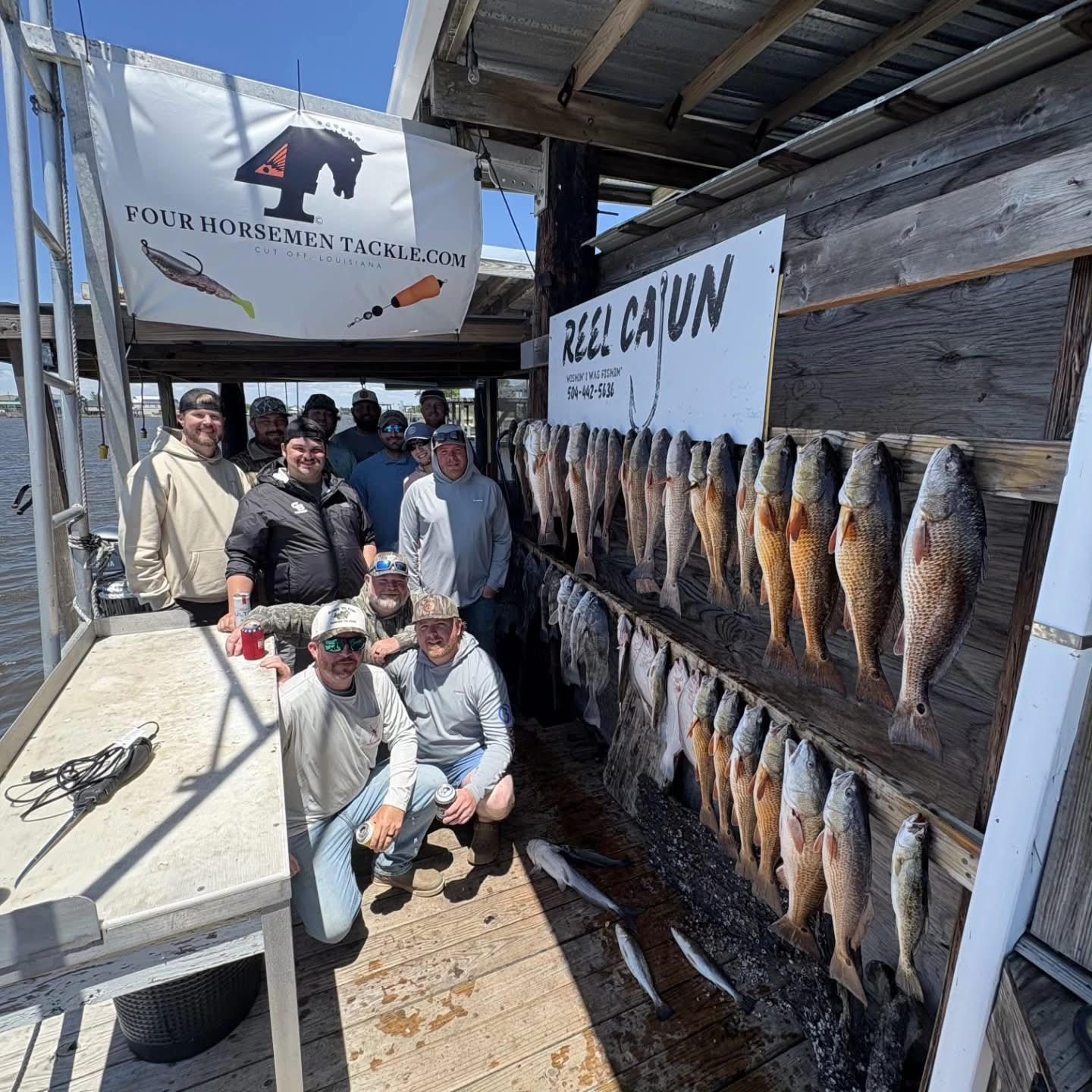 People posing beside rows of hanging fish at a dockside fish display