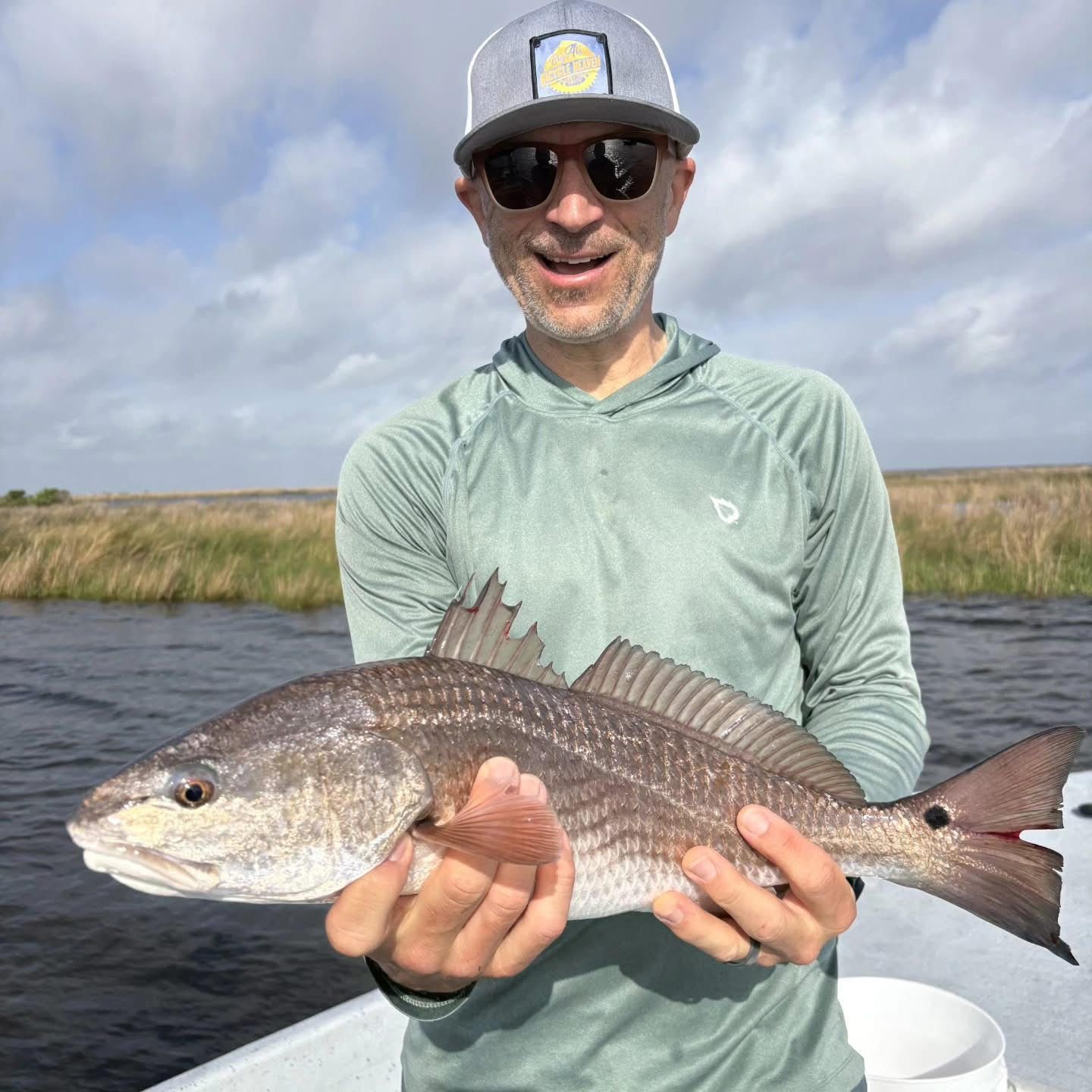 Man holding a large fish on a boat in calm water under a cloudy sky.