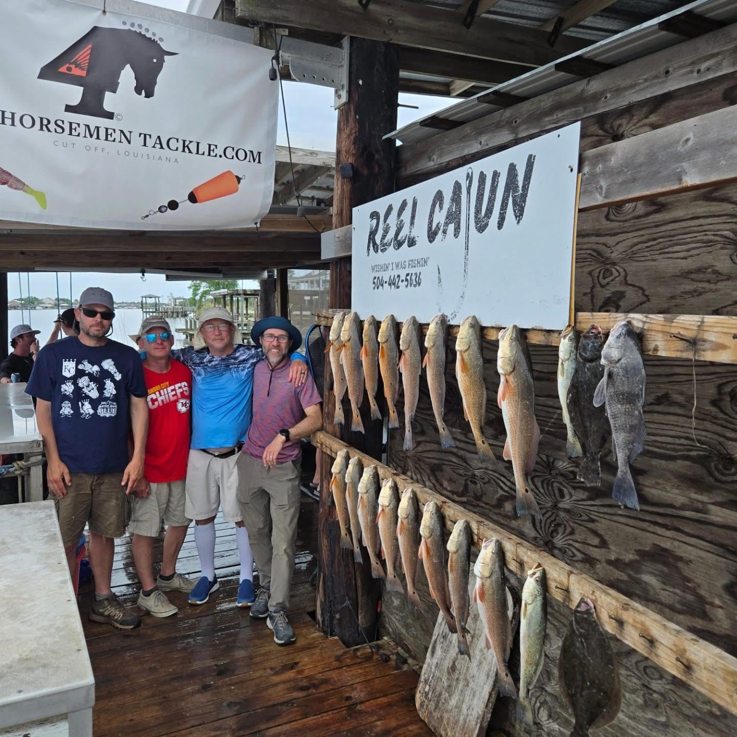 Five people posing at a rustic fish market display with hanging fish and a 