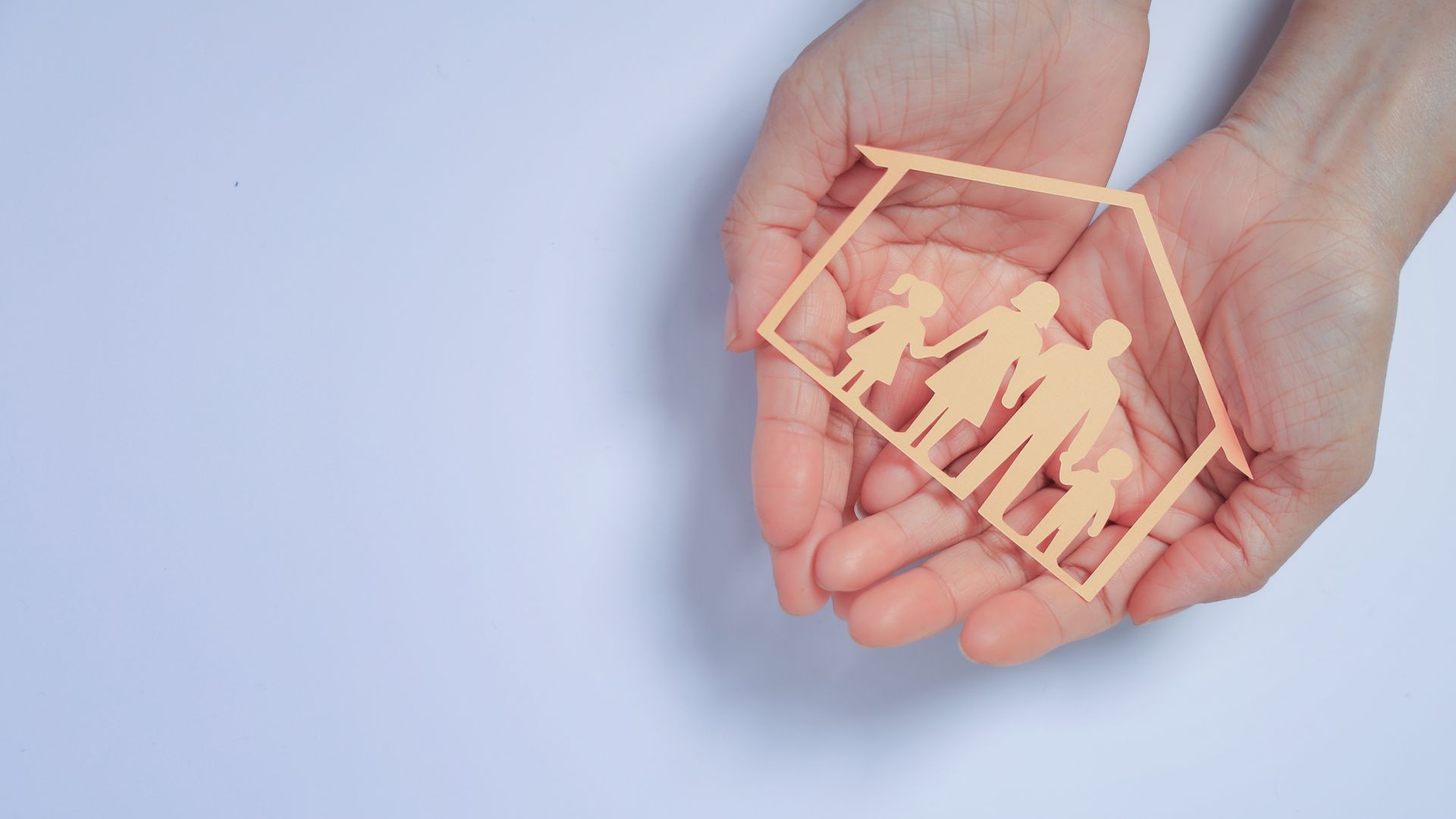 Couple smiles, shaking hands with a person in a light gray suit at a table. Bright office setting.