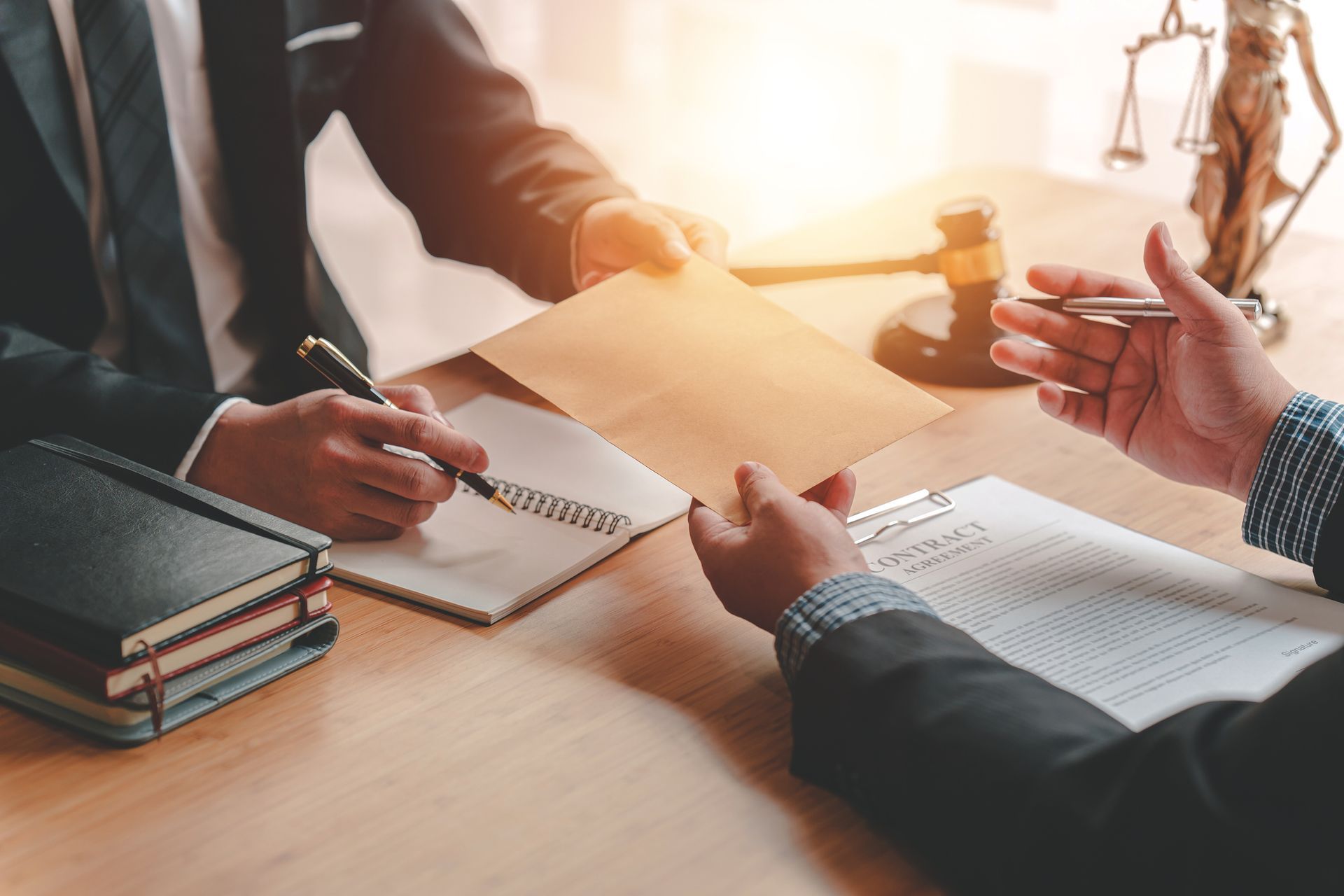 Two people in suits exchanging an envelope across a desk; legal documents, a gavel, and scales are visible.
