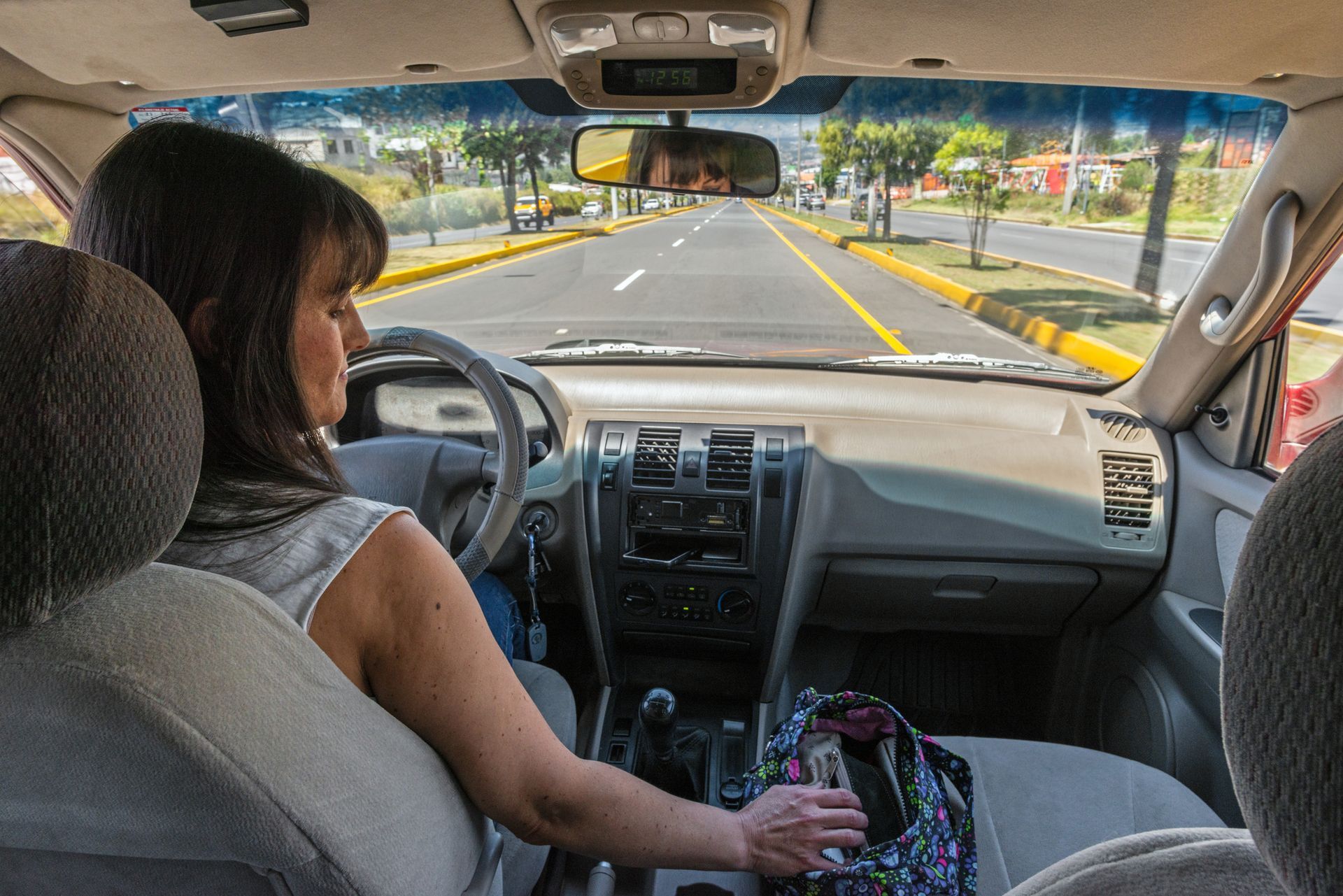 Woman driving a car on a road, arm reaching towards the center console.