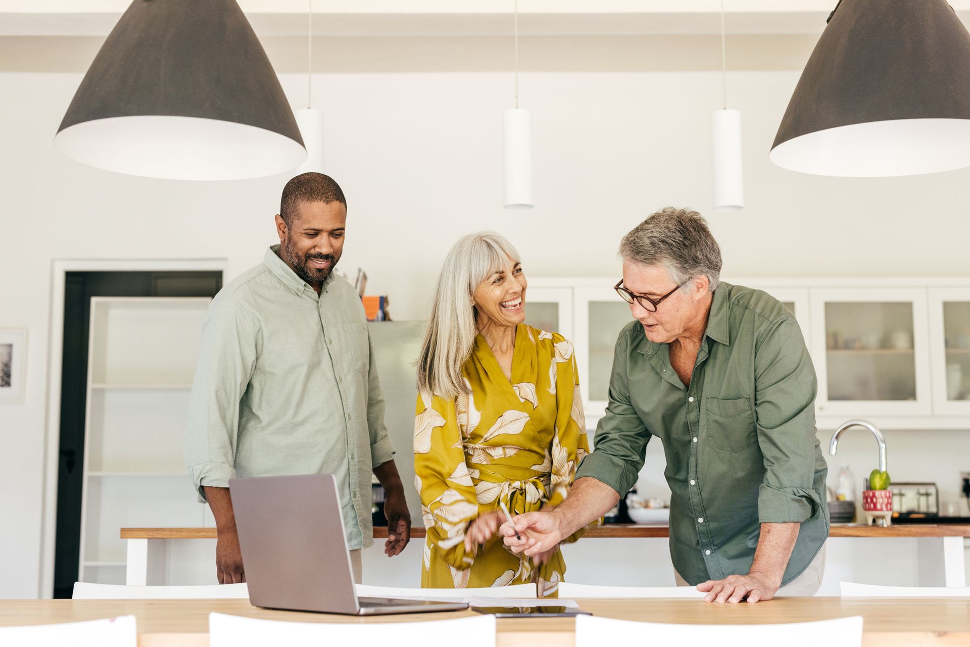Three people looking at laptop and paperwork at a table in a kitchen. Three people looking at laptop and paperwork at a table in a kitchen.