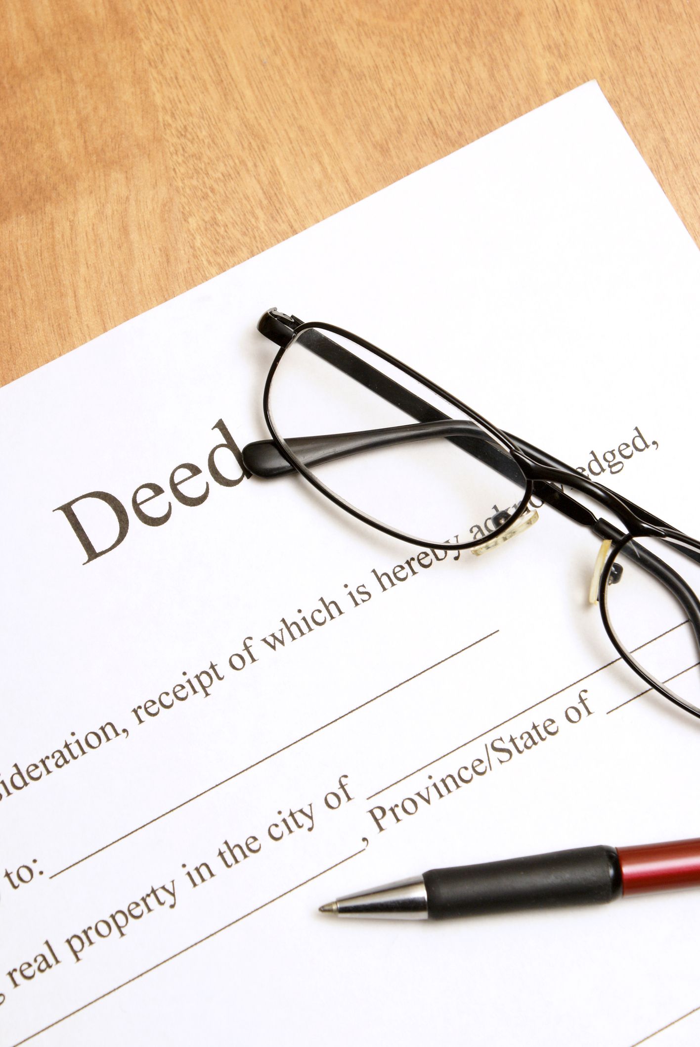 Deed document with eyeglasses and a pen on a wooden surface.