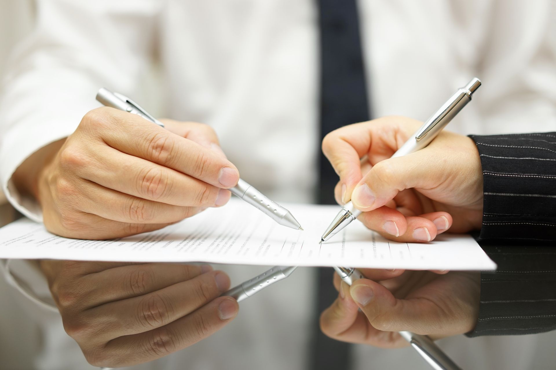 Two people signing a document with silver pens on a reflective black surface.