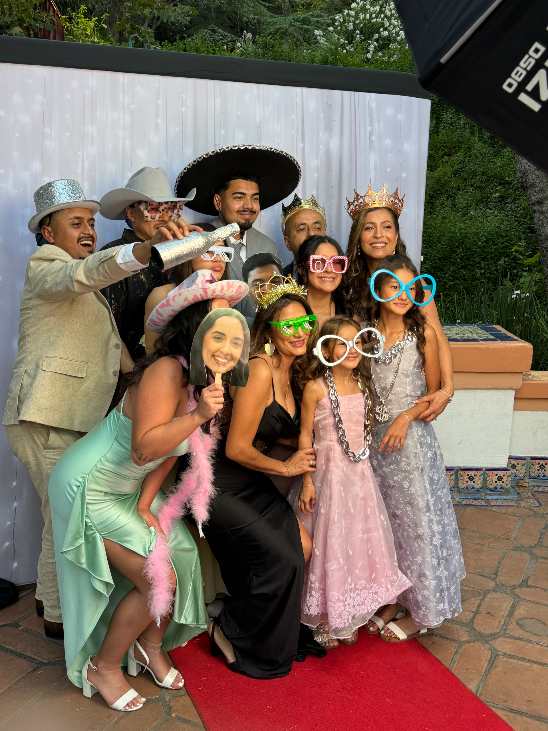 Group posing at a photo booth with props, red carpet, and white backdrop. People smiling, wearing costumes