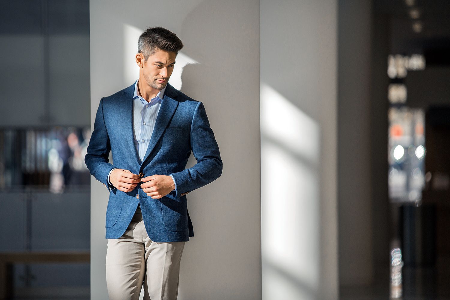 A man in a blue suit is standing next to a wall adjusting his jacket.