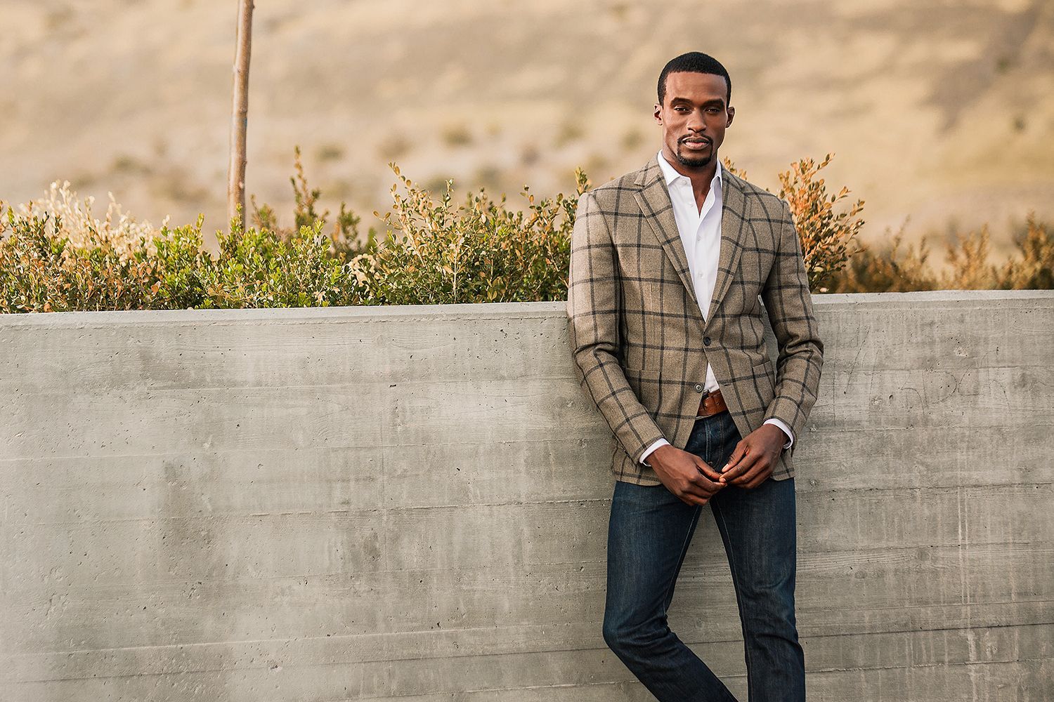 A man in a suit is leaning against a concrete wall.