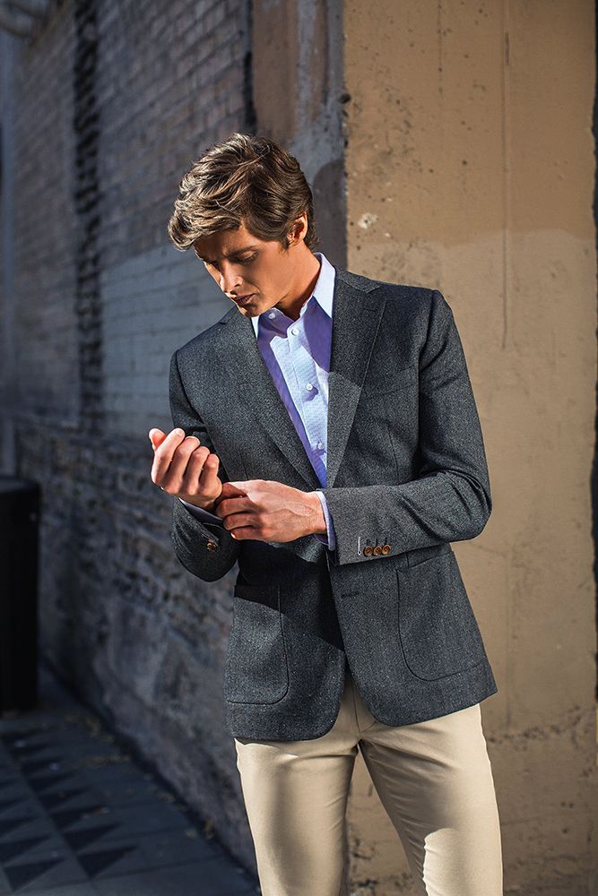 A man in a suit is standing next to a brick wall adjusting his jacket.