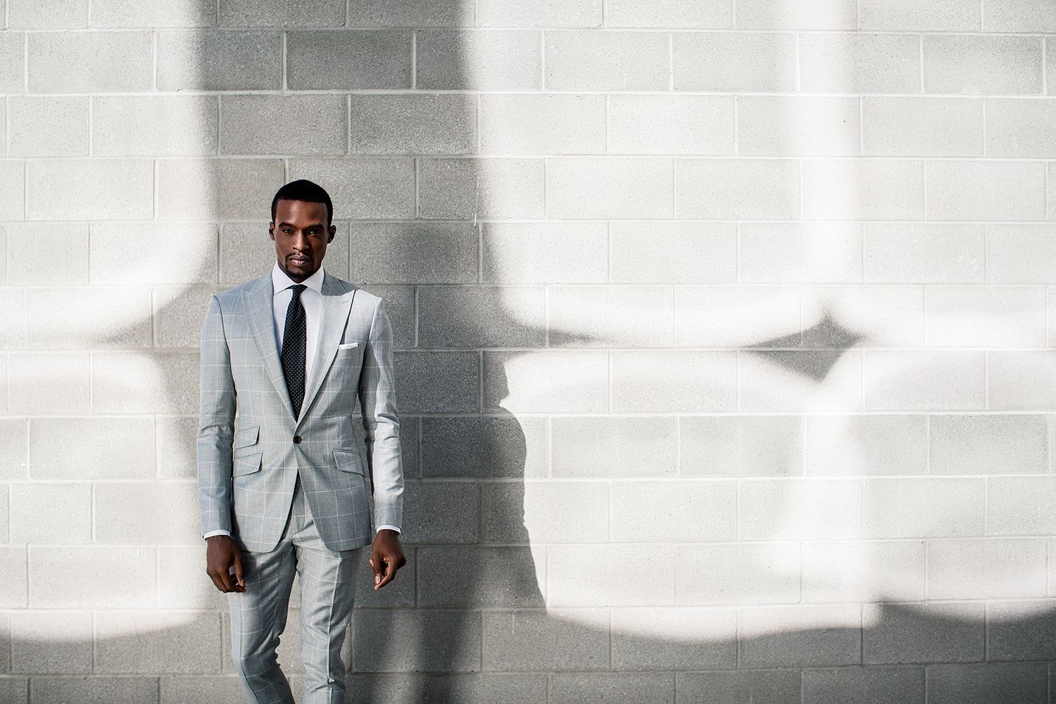 A man in a suit and tie is standing in front of a brick wall.