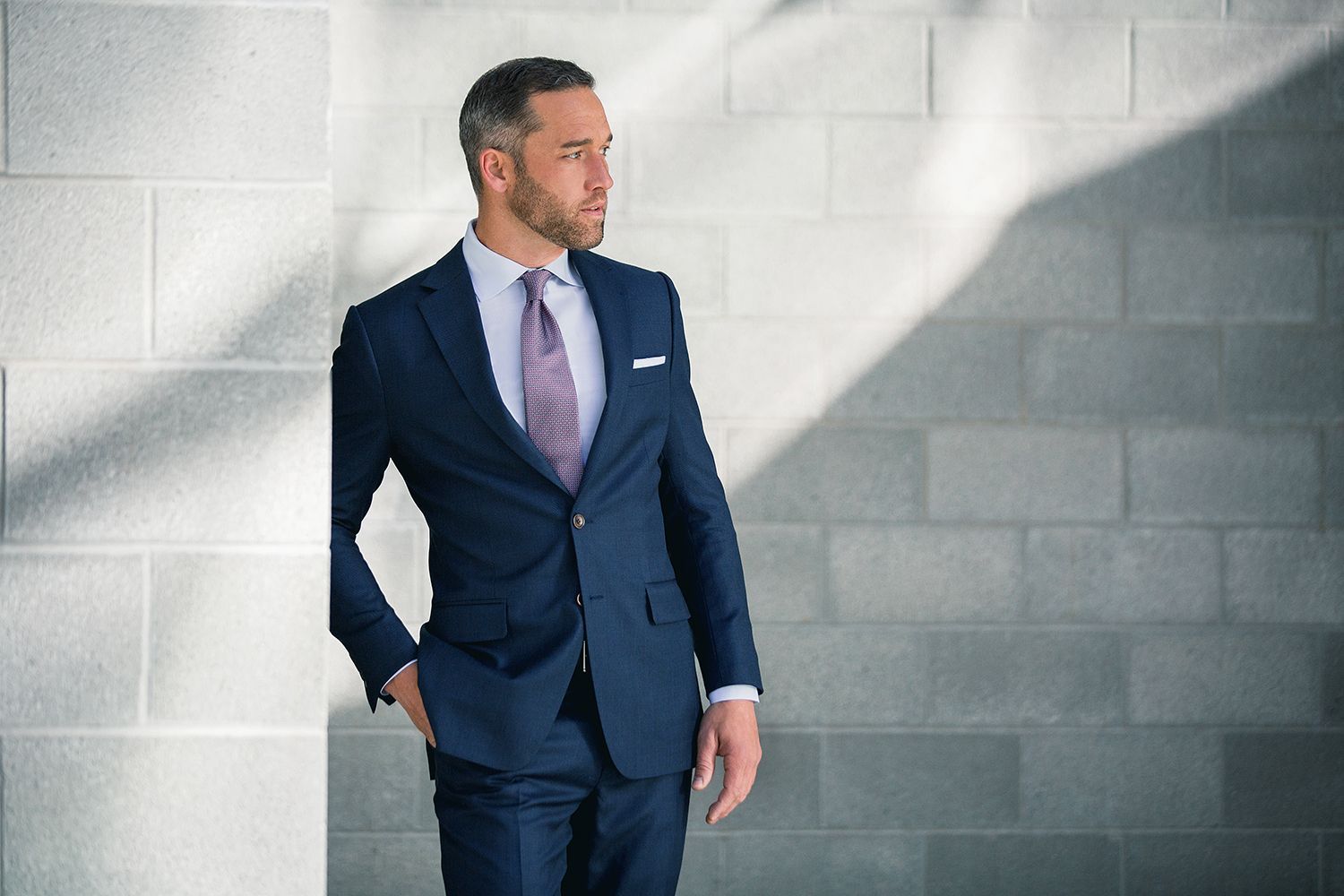 A man in a suit and tie is leaning against a brick wall.