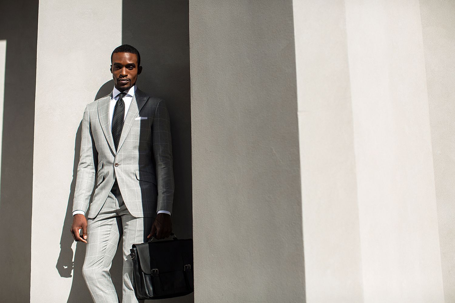 A man in a suit and tie is standing next to a wall holding a briefcase.
