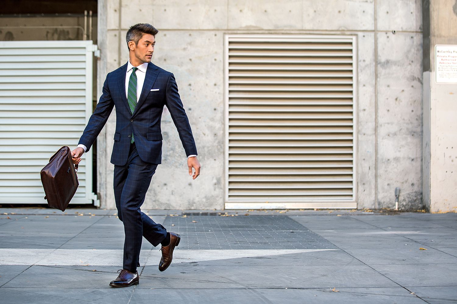a man in a suit and tie is walking down the street holding a briefcase .