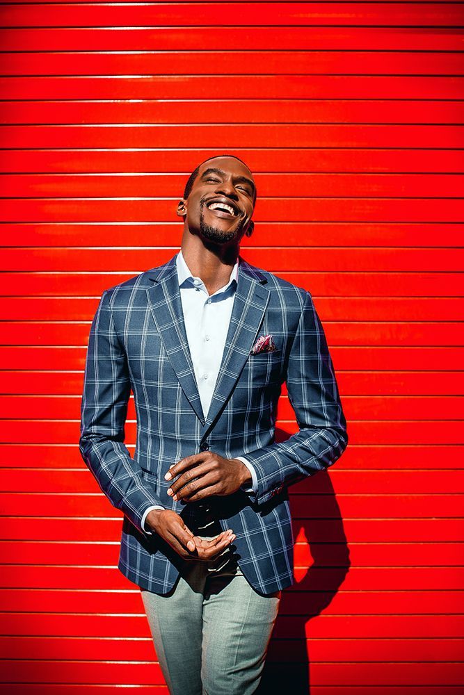 a man in a suit is standing in front of a red wall .