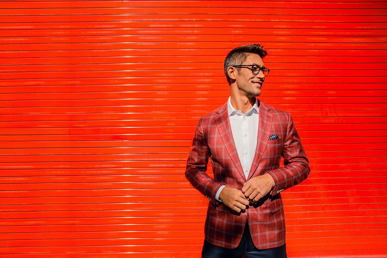 a man in a red jacket and glasses is standing in front of a red wall .