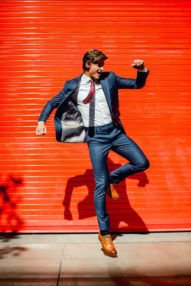 A man in a suit and tie is jumping in the air in front of a red garage door.