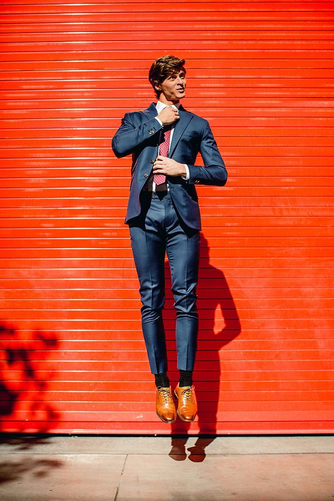 A man in a suit and tie is jumping in the air in front of a red garage door.