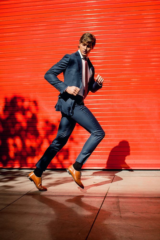 a man in a suit and tie is jumping in the air in front of a red wall .