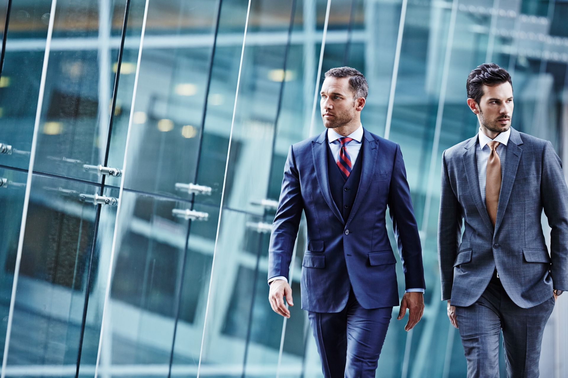 Two men in suits and ties are walking in front of a building.