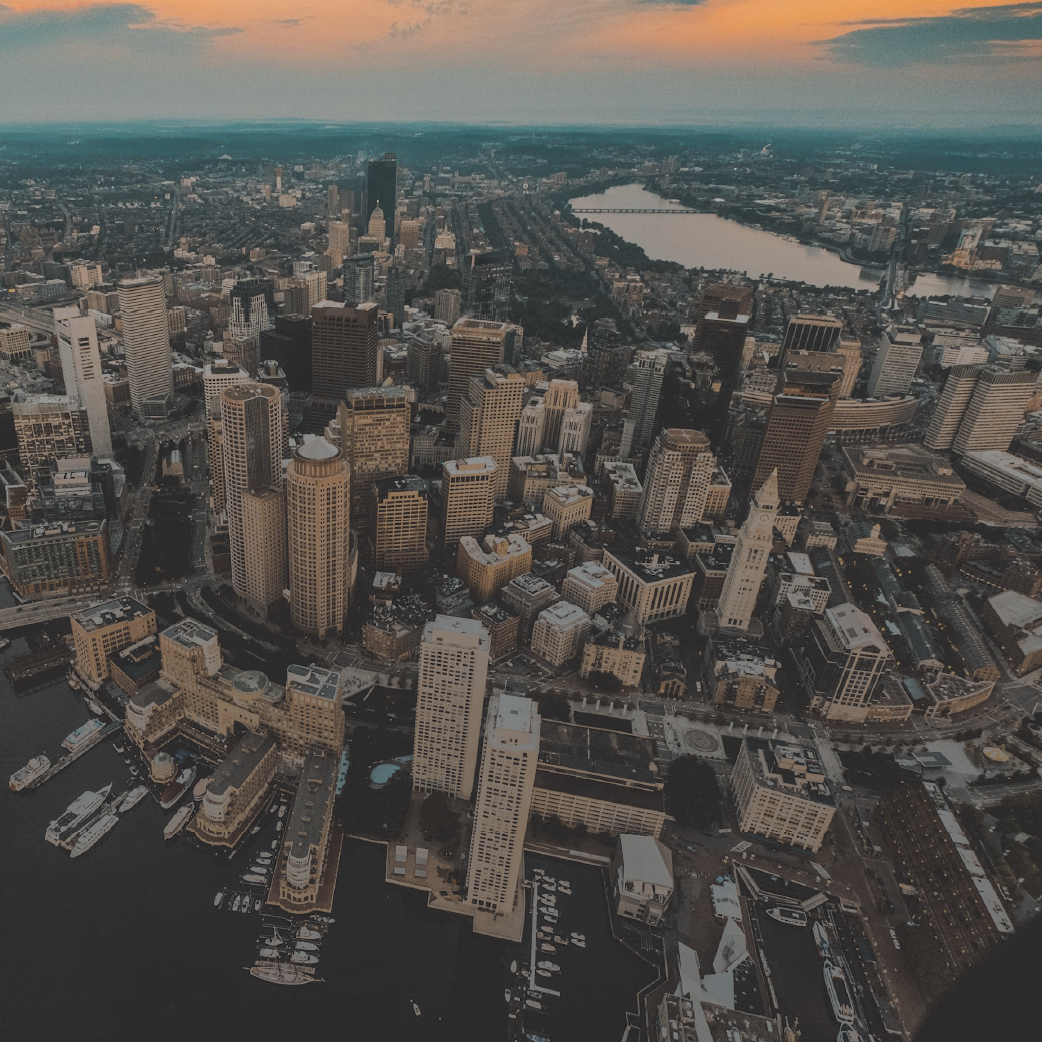 Aerial view of a city with tall buildings, waterfront, and a body of water in the background at sunset.