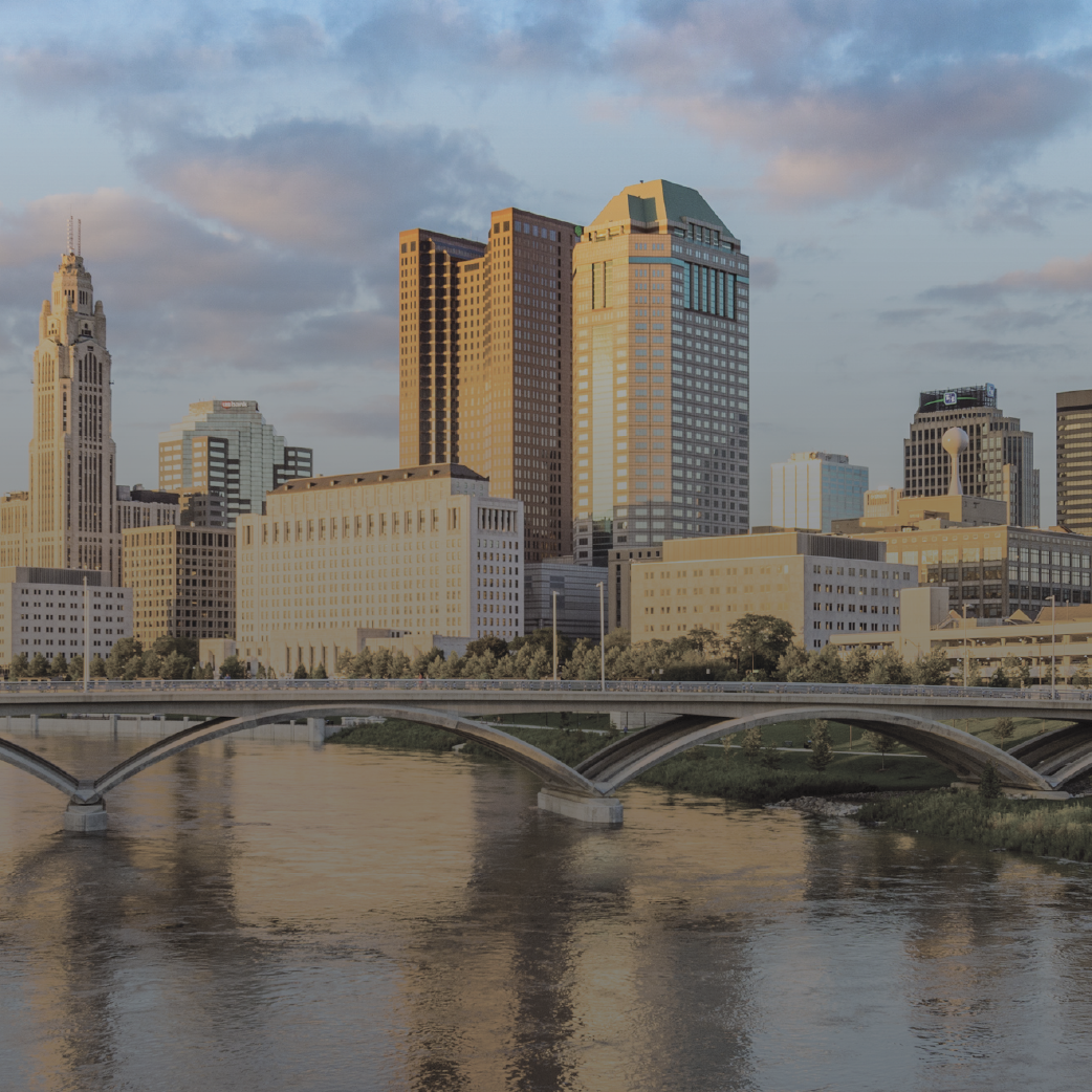 Skyline of Columbus, Ohio, featuring the Scioto River, bridges, and tall buildings, under a pastel sky.