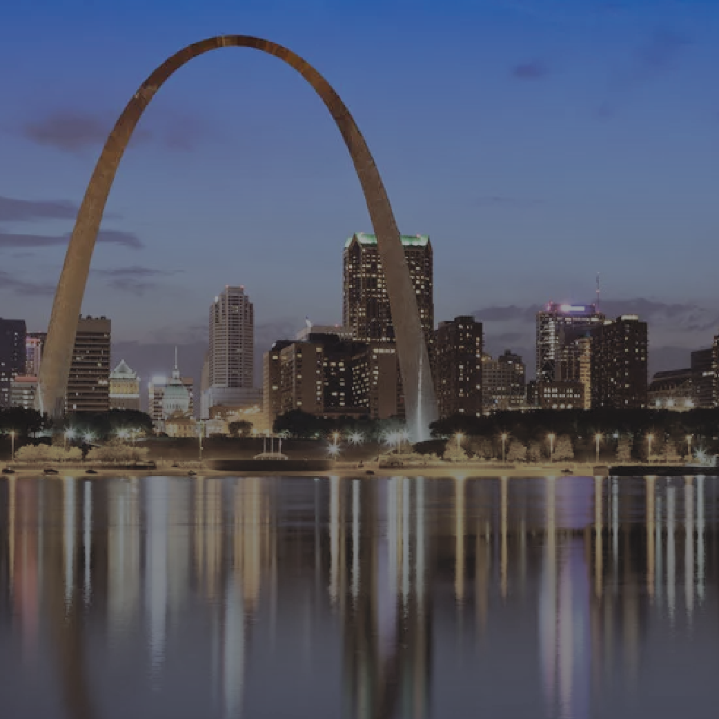 St. Louis Arch and city skyline reflected in water at dusk.