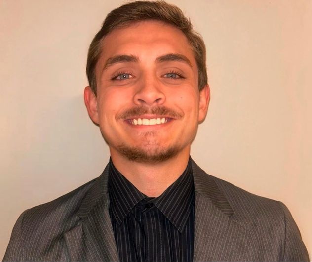 A young man with a beard and mustache is smiling for the camera.