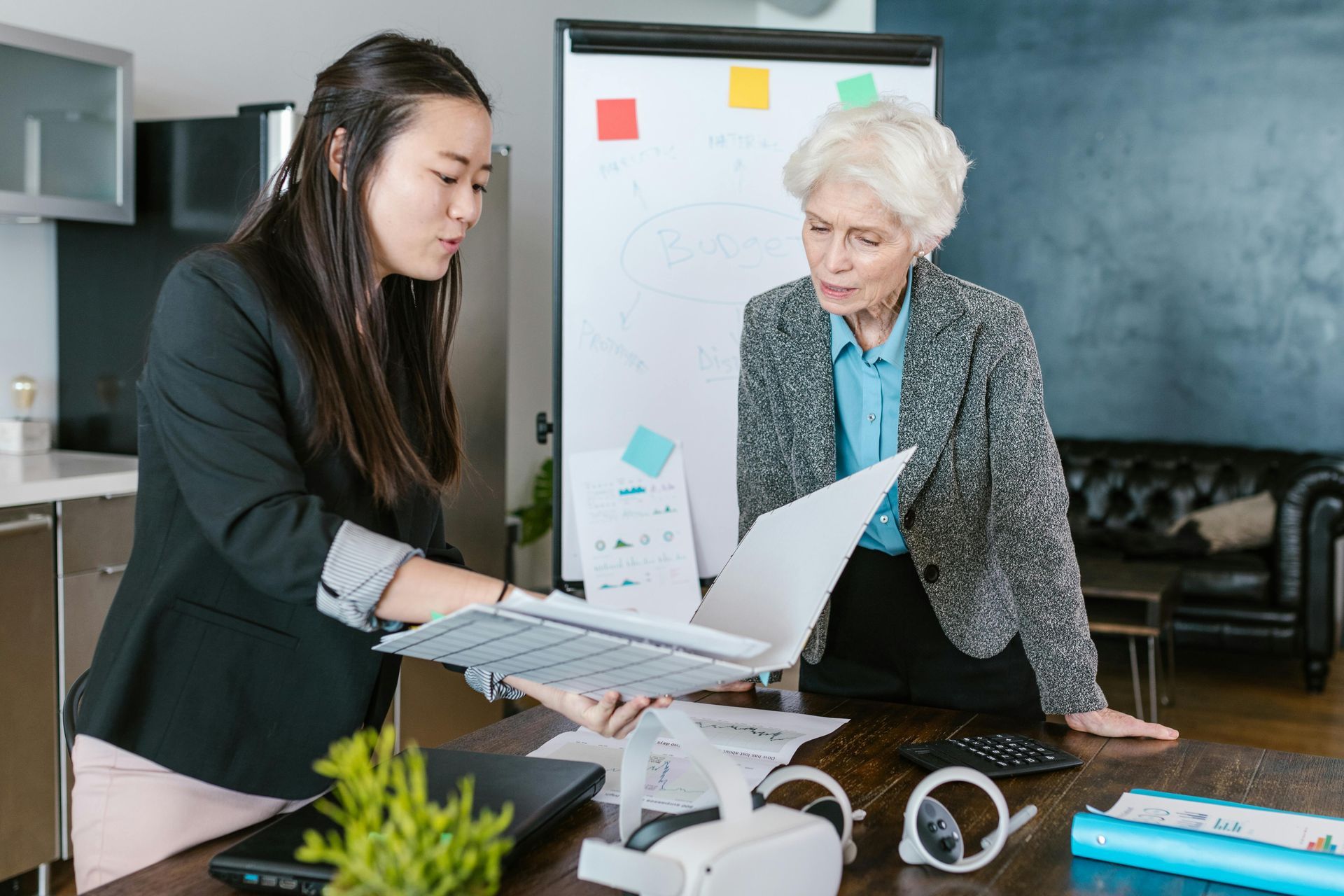 Two women are standing at a table looking at papers.
