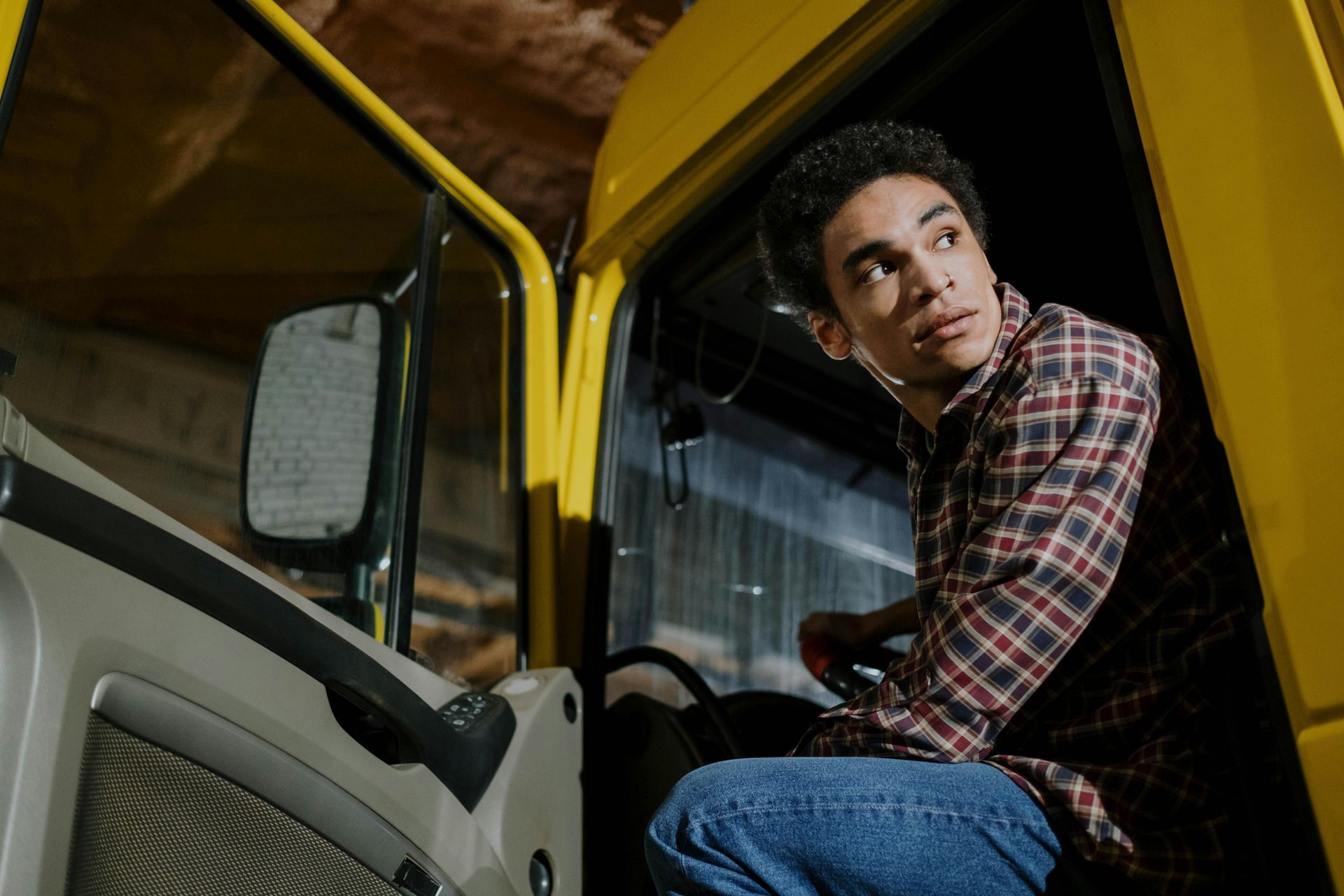 A man in a plaid shirt is sitting in the driver 's seat of a yellow truck.